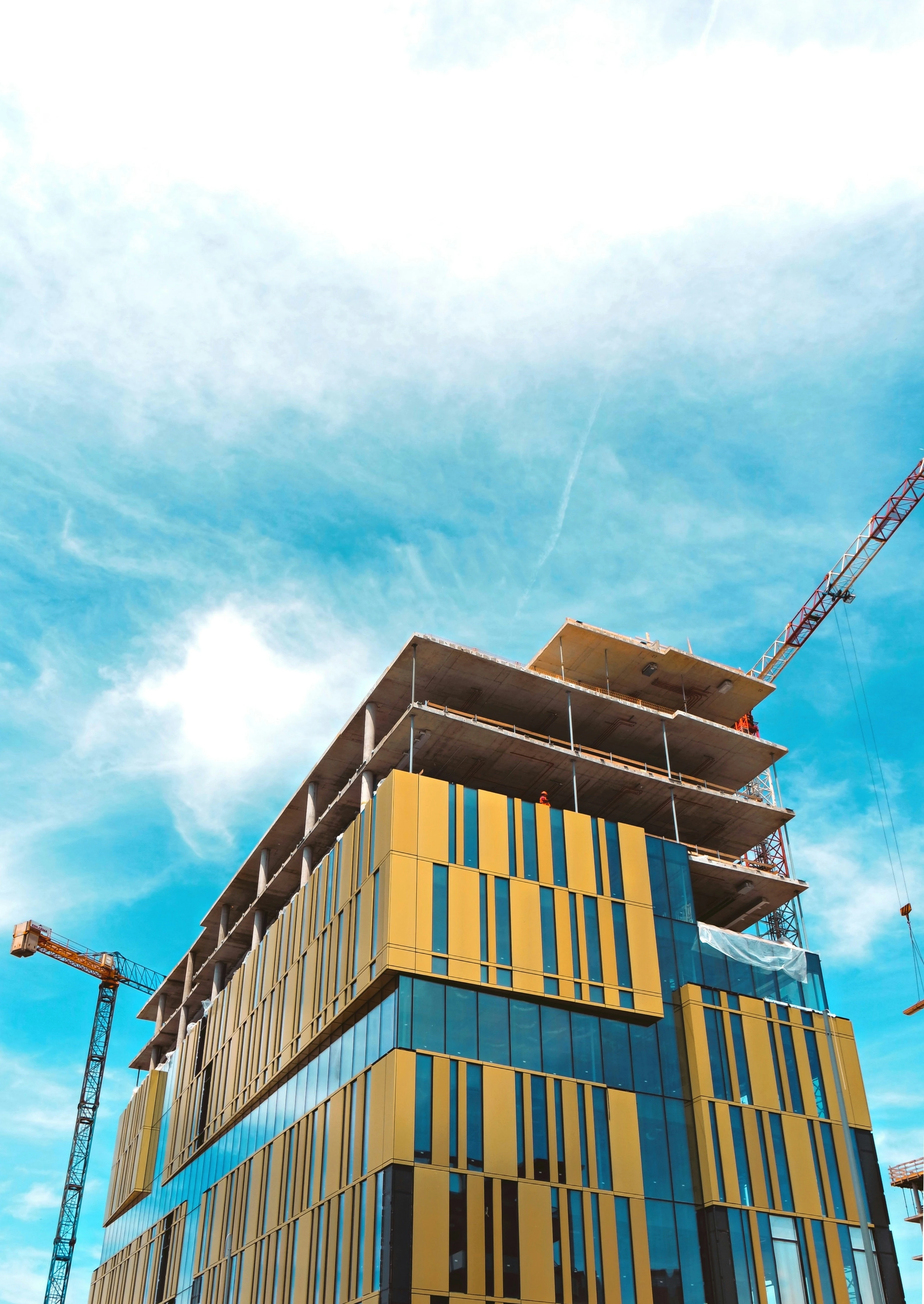 Modernes Gebäude im Bau mit Kränen vor blauem Himmel